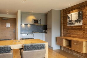 Een moderne keuken met een magnetron, oven en een inbouwvaatwasser. Er is een eettafel met stoelen en een houten kast met lades.