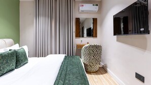 Hotelkamer met een bed, een stoel, een spiegel, een wandairconditioner en een raam met gordijnen.