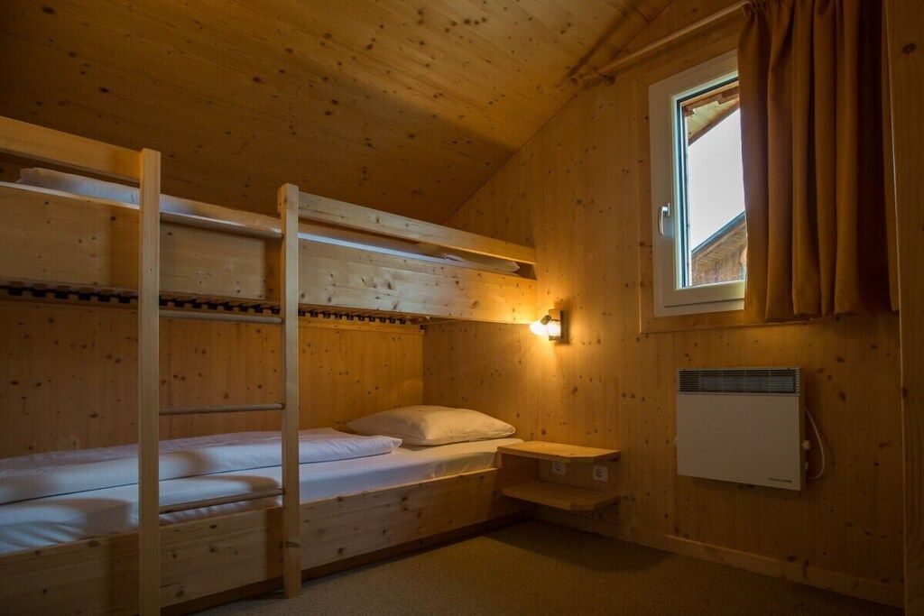 Een slaapkamer met stapelbed, een raam, een wandheater en een klein plankje.
