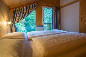 Ein Zimmer mit einem Bett, einem Vorhangfenster und Blick auf Bäume.