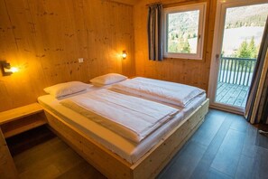Um quarto de madeira com uma cama, janela e varanda.