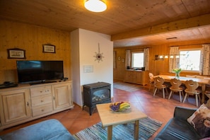L’intérieur chaleureux d’un chalet comprend une télévision, une cheminée, un coin repas avec des chaises en bois et un canapé.