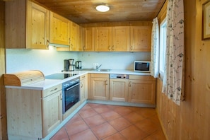 A compact kitchen with wooden cabinets, a built-in oven, a microwave, and a sink. - Cabin in Annaberg with swimming pool (Annaberg)
