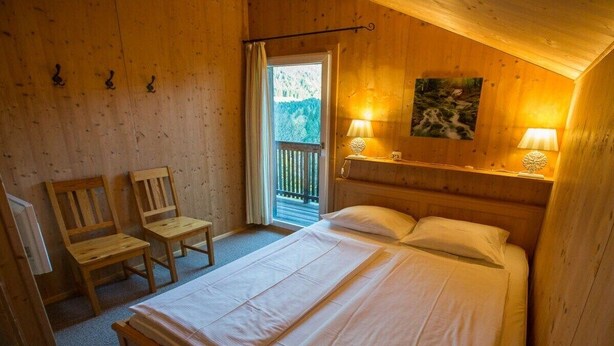 Una habitación de madera con una cama, dos sillas, una mesita y un cuadro en la pared.