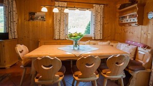 Un comedor de madera con una mesa y sillas, un florero con flores y una ventana con cortinas.