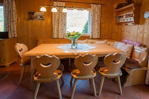 A wooden dining room with a table and chairs, a vase with flowers, and a window with curtains. - Cabin in Annaberg with swimming pool (Annaberg)