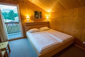 Une pièce en bois avec un lit, deux lampes de chevet, un tableau et une vue sur l’extérieur.