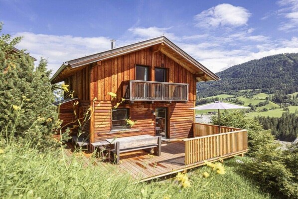 Eine Holzhütte mit Balkon, einer Terrasse und Blick auf eine gebirgige Landschaft.