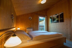 Ein Zimmer mit Holzboden, einem Bett, einem Fenster und einem an der Wand hängenden Bild.