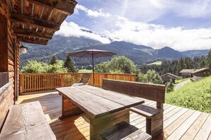 Eine Holzdiele mit Tisch und Bänken, mit Blick auf eine gebirgige Landschaft.