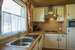 Eine Küche mit einer Edelstahl-Spüle, Holzschränken, einem Herd und einem Fenster mit Vorhängen.