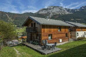 Una baita in legno con un balcone, una terrazza con sedie e vista sulle montagne.