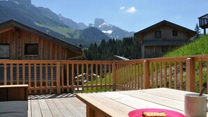 A wooden deck with a table and chairs, overlooking a mountainous landscape with cabins. - Cabin in Annaberg with swimming pool (Annaberg)
