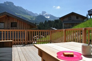 A wooden deck with a table and chairs, overlooking a mountainous landscape with cabins. - Cabin in Annaberg with swimming pool (Annaberg)
