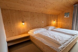 Une pièce en bois avec un lit, deux lampes fixées au mur et un petit tableau accroché au mur.