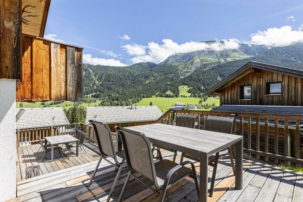 Een houten terras met een tafel en stoelen, met uitzicht op een bergachtig landschap.