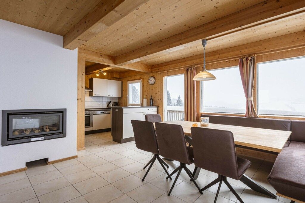 Een moderne keuken met houten balken, een eethoek met een tafel en stoelen, en een open haard.