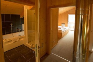 Innenansicht einer Holzhütte mit Badezimmer, Bett und sichtbarem Schornstein.