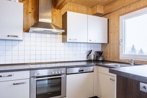 A modern kitchen with white cabinets, stainless steel appliances, and a window with a view of trees. - Cabin in Annaberg with swimming pool (Annaberg)