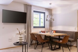 Een moderne eetruimte met een tafel, stoelen, een bank, een televisie en een raam met gordijnen.