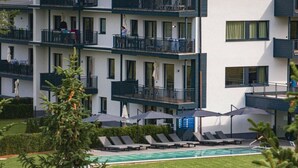 Um hotel com vários andares, varandas, piscina e espreguiçadeiras.