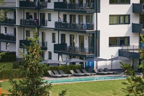 Un hotel a più piani con balconi, piscina e sdraio.