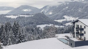 Um edifício moderno com piscina, cercado por montanhas e árvores cobertas de neve.