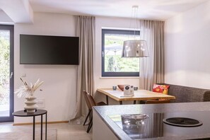 A modern kitchen with a central island, a dining area with a table and chairs, a flat-screen TV mounted on the wall, and a window with curtains. - Holiday apartment for 6 people & infinity pool (St. Martin am Tennengebirge)