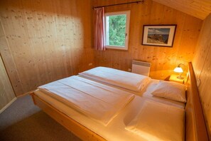 Een houten kamer met een bed, een raam met gordijn en een foto aan de muur.