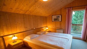 A wooden cabin room with a bed, bedside lamps, and a window with curtains. - Cabin in Annaberg with swimming pool (Annaberg)