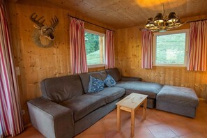 A cozy cabin interior with a sectional sofa, a small wooden table, and a mounted deer head on the wall. - Cabin in Annaberg with swimming pool (Annaberg)