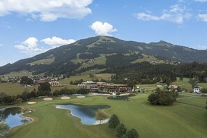 A golf course with a mountain backdrop, a clubhouse, and a small pond. - Superior 2-bedroom apartment (Westendorf)