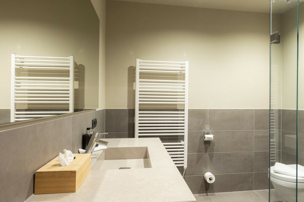 A modern bathroom with a rectangular sink, two towel racks, a glass shower enclosure, and a wooden tissue box.