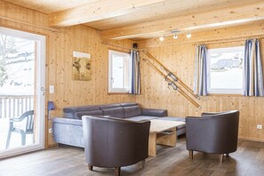 Ein Holzinterieur mit einer Couch, zwei Sesseln, einem Tisch und einem Skiständer.