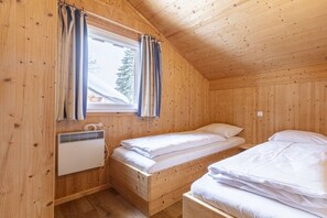 A wooden cabin room with two beds, a window with curtains, and a radiator. - Cabin in Annaberg with swimming pool (Annaberg)