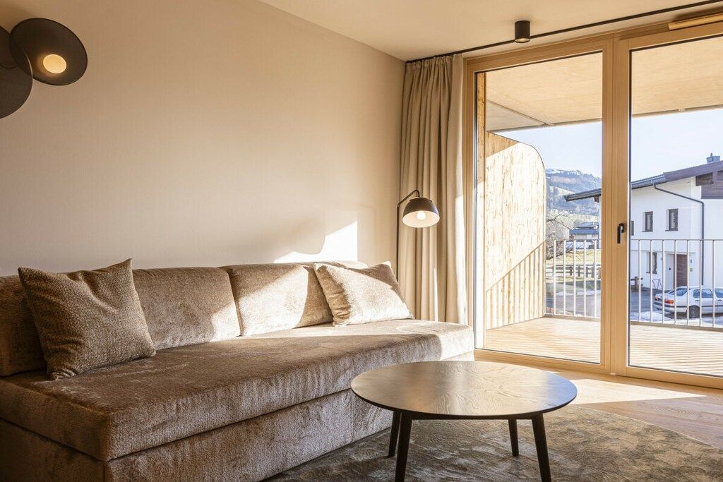 Un salon moderne avec un canapé, une table basse ronde et une grande porte-fenêtre coulissante donnant sur un balcon extérieur.