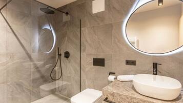 Une salle de bain moderne avec une douche à parois de verre, des toilettes blanches, un lavabo en marbre et un grand miroir.