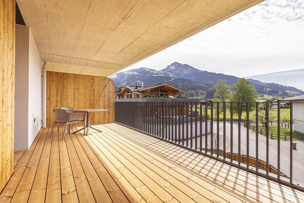 A wooden deck with a table and chairs, overlooking a mountainous landscape.