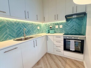 Eine Küche mit weißen Schränken, einer Fischgrät-Fliesenrückwand, einer Edelstahl-Spüle, einem Wasserkocher, einem Toaster und einem schwarzen Backofen.