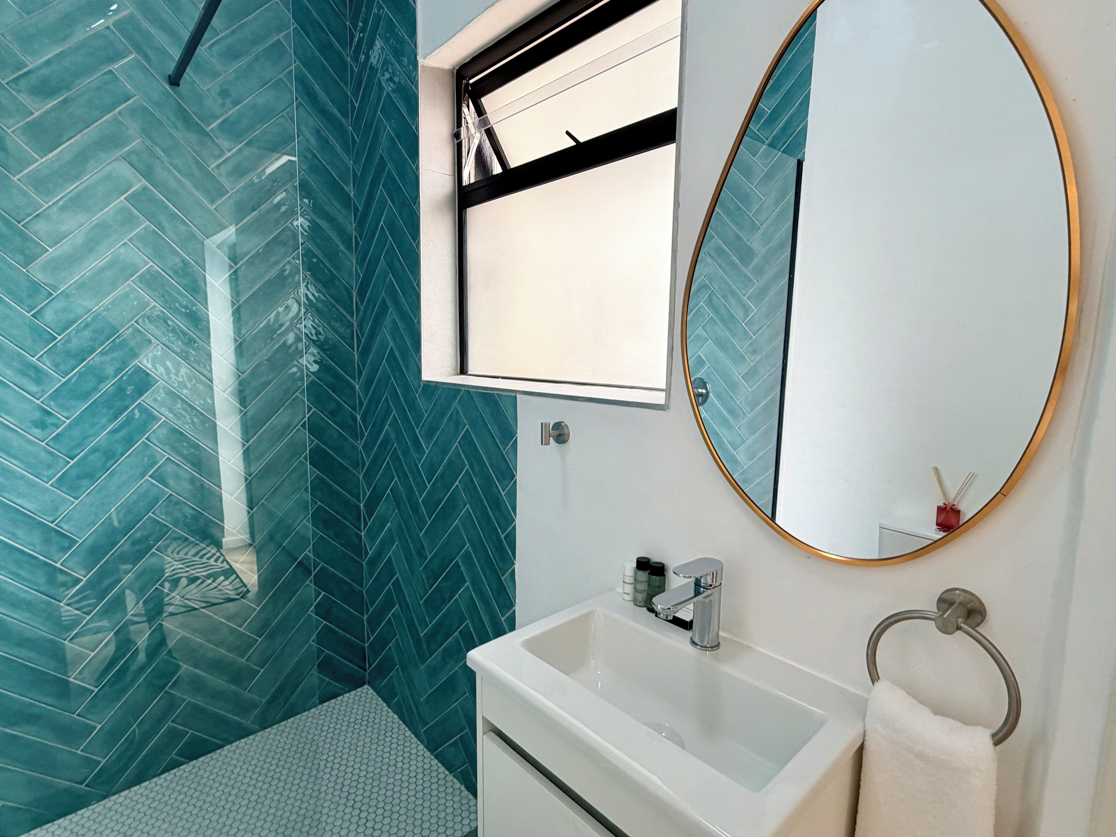 A bathroom with a herringbone tile pattern, a white sink, a mirror with a gold frame, and a towel rack.
