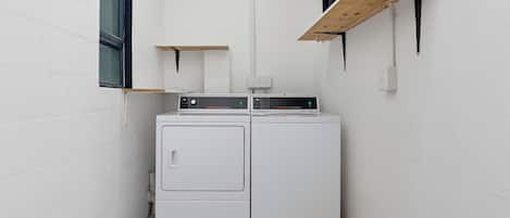 A laundry room with two stacked washers and dryers, wooden shelves, and a window.