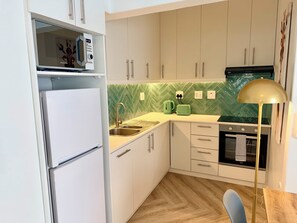 Eine kompakte Küche mit Kühlschrank, Spüle, Schränken, Mikrowelle, Wasserkocher, Toaster und Herd.