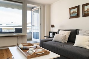 A modern living room with a grey sofa, a wooden coffee table with cups and a tray, a lamp, and two framed pictures on the wall. - Holiday apartment with 1 bedroom (Westerland)