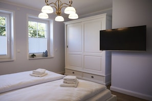 Ein Hotelzimmer mit zwei Betten, einem großen Kleiderschrank, einem an der Wand befestigten Fernseher und einem Fenster mit Jalousien.