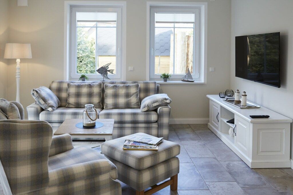 A living room with a sofa, ottoman, and coffee table, a television on the wall, and a window with a view.