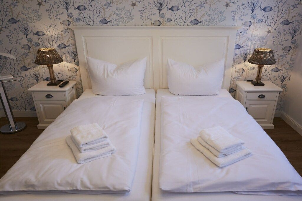 Un lit double avec du linge de lit blanc et des oreillers, deux lampes de chevet et un papier peint à motifs floraux.