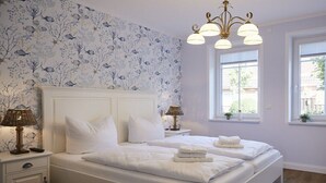 A bedroom with a large bed, two bedside tables with lamps, a chandelier, and a window with a view. - Holiday apartment in Büsum with swimming pool (Büsum)