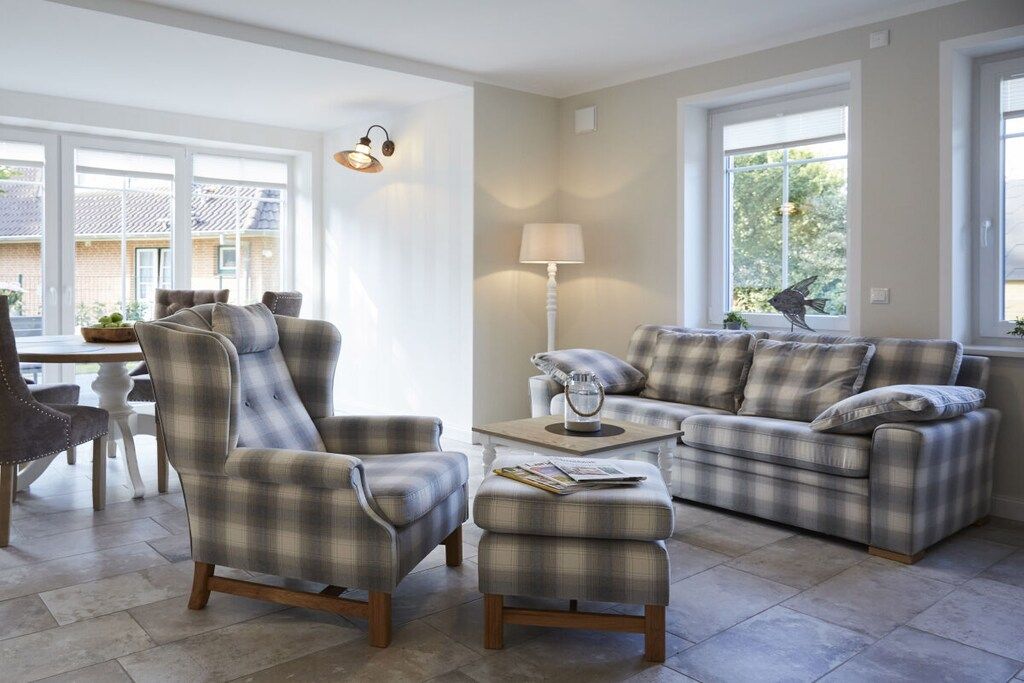 A living room with a sofa, armchair, ottoman, and a lamp.