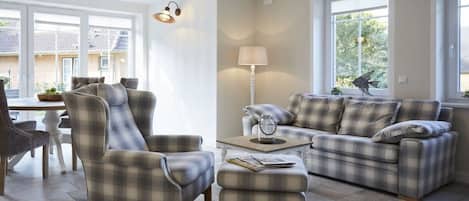 A living room with a sofa, armchair, ottoman, and a lamp.