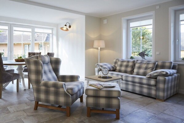 Een woonkamer met een bank, fauteuil, voetenbankje en een lamp.